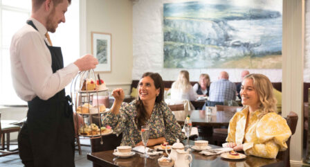 Guests enjoying afternoon tea in a cosy hotel dining room with a waiter serving pastries.