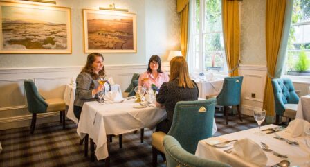 Three friends enjoy dining in a cosy, elegant hotel restaurant with warm decor and large windows.