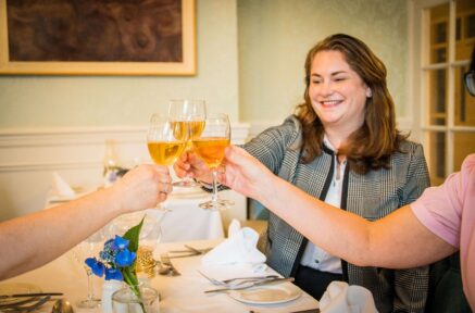 A group toasting with drinks at a bright, elegant hotel dining room, creating a warm atmosphere.