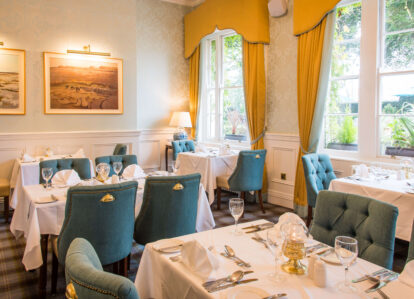 Elegant restaurant dining area with blue chairs, white tablecloths, and warm natural light.