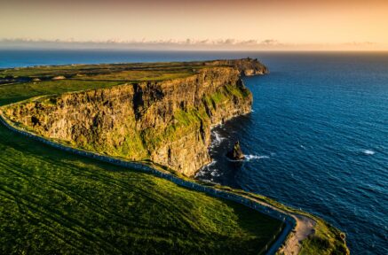 Scenic view of the Cliffs of Moher at sunset with lush green fields and expansive ocean.