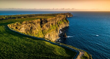 Scenic view of the Cliffs of Moher at sunset with lush green fields and expansive ocean.