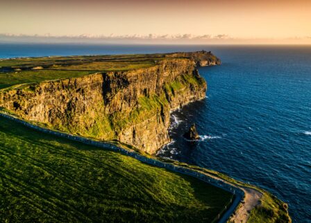 Scenic view of the Cliffs of Moher at sunset with lush green fields and expansive ocean.