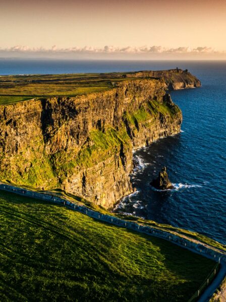 Scenic view of the Cliffs of Moher at sunset with lush green fields and expansive ocean.