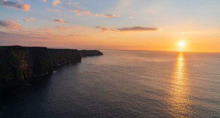 Breathtaking sunset over the Cliffs of Moher, with golden skies reflecting on the ocean.