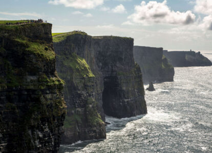 People admire the stunning Cliffs of Moher, standing on lush green cliffs overlooking the ocean.