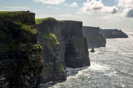 People admire the stunning Cliffs of Moher, standing on lush green cliffs overlooking the ocean.