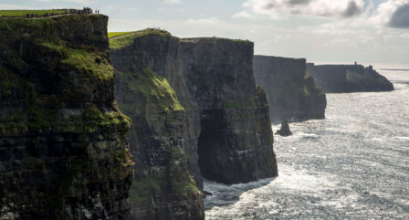 People admire the stunning Cliffs of Moher, standing on lush green cliffs overlooking the ocean.