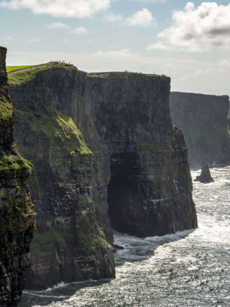 People admire the stunning Cliffs of Moher, standing on lush green cliffs overlooking the ocean.