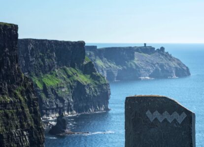 Stunning Cliffs of Moher, viewed on a sunny day, with the ocean and a stone marker in the foreground.