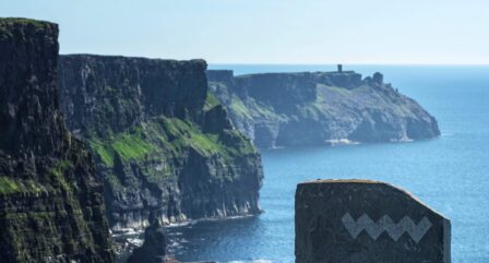 Stunning Cliffs of Moher, viewed on a sunny day, with the ocean and a stone marker in the foreground.