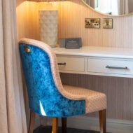 Cosy hotel room with a velvet blue chair, a stylish lamp, and a welcoming atmosphere.