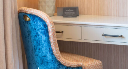 Cosy hotel room with a velvet blue chair, a stylish lamp, and a welcoming atmosphere.