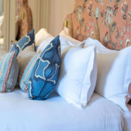 Elegant hotel room with white and blue pillows on a neatly made bed, floral-patterned headboard.