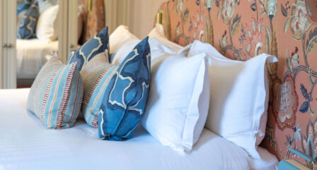 Elegant hotel room with white and blue pillows on a neatly made bed, floral-patterned headboard.