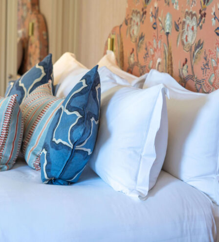 Elegant hotel room with white and blue pillows on a neatly made bed, floral-patterned headboard.