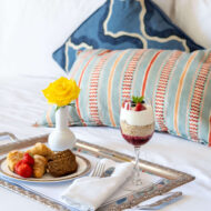 Luxurious breakfast with pastries and parfait on hotel bed with vibrant cushions.