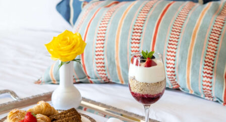 Luxurious breakfast with pastries and parfait on hotel bed with vibrant cushions.