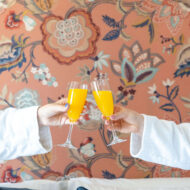 Couple enjoying mimosas in a cosy hotel room with floral decor.
