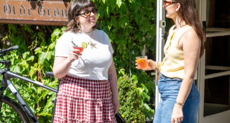 Two friends enjoy drinks outside the ivy-covered Old Ground Hotel on a sunny day.