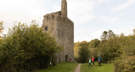 A family explores a historic stone tower surrounded by lush greenery on a sunny day.