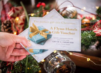 Hand holding a Flynn Hotels gift voucher with festive decorations in the background.