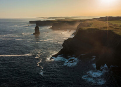 Majestic coastal cliffs at sunset with waves gently lapping the rugged shoreline, creating a serene atmosphere.