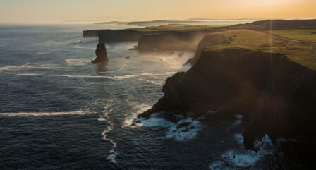 Majestic coastal cliffs at sunset with waves gently lapping the rugged shoreline, creating a serene atmosphere.