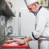 Chef preparing meat in a kitchen at Old Ground Hotel, creating a warm dining experience.