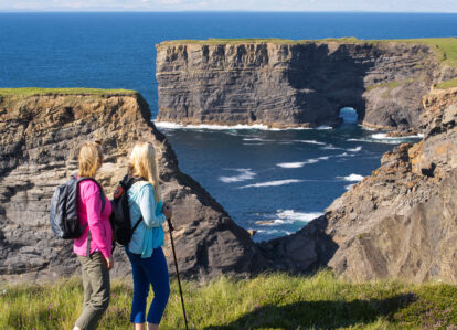 Couple hiking on coastal cliffs with ocean backdrop near Old Ground Hotel.
