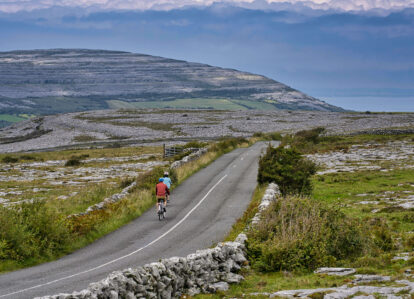 A couple cycling on a scenic, rural road with lush hills and expansive landscapes.