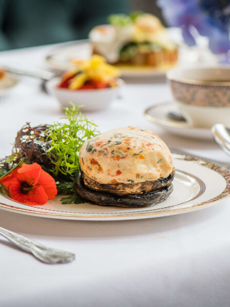 Elegant breakfast setting with gourmet dish, fresh pastries, and tea on a white tablecloth.