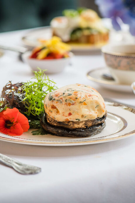 Elegant breakfast setting with gourmet dish, fresh pastries, and tea on a white tablecloth.