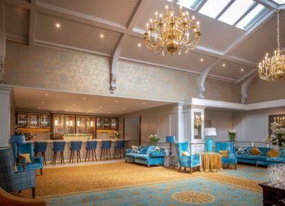Elegant hotel lounge with blue seating, a family enjoying drinks at the bar, under golden chandeliers.