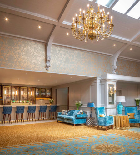 Elegant hotel lounge with blue seating, a family enjoying drinks at the bar, under golden chandeliers.