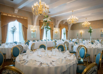 Elegant hotel dining room with round tables, set for a banquet, featuring chandeliers and floral decor.