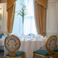 Elegant dining setup in cosy hotel setting with golden curtains and floral arrangement.