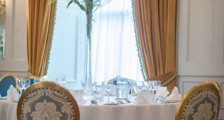Elegant dining setup in cosy hotel setting with golden curtains and floral arrangement.