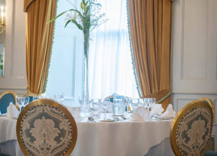 Elegant dining setup in cosy hotel setting with golden curtains and floral arrangement.