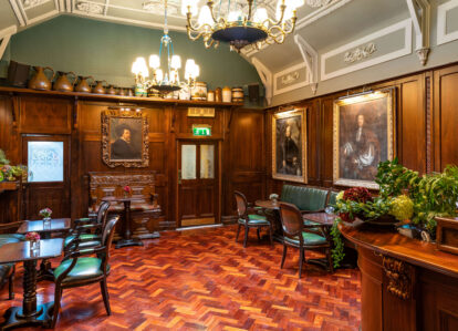 Elegant hotel lounge with wooden decor, floral accents, and framed portraits on the walls.