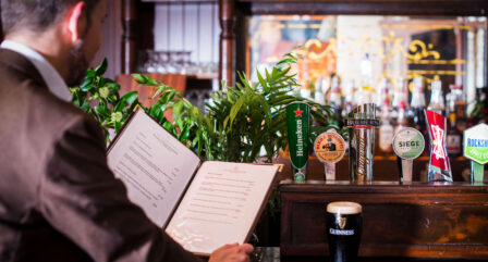 A guest reviews the menu at a cosy hotel bar with lush greenery and a pint of Guinness.
