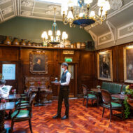 Elegant hotel lounge with vintage decor, a guest reading, and a waiter serving drinks.