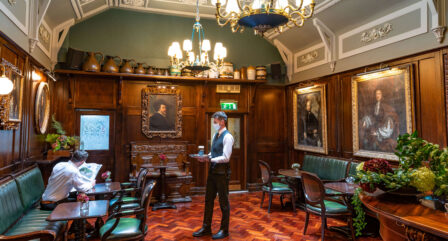 Elegant hotel lounge with vintage decor, a guest reading, and a waiter serving drinks.