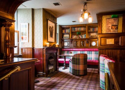 Cosy hotel lounge with plaid seating, warm lighting, and a fireplace, perfect for relaxing moments.