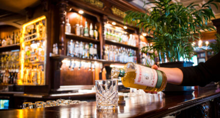 Cosy hotel pub, hand pouring Irish whiskey into crystal glass. Warm, inviting atmosphere.