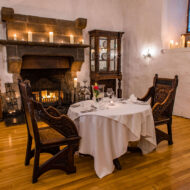 Cosy dining room with a table for two by a lit fireplace, adorned with candles.