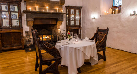 Cosy dining room with a table for two by a lit fireplace, adorned with candles.