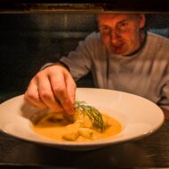 Chef garnishing a gourmet dish with fresh herbs in a warm, inviting kitchen setting.