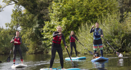 A joyful group paddleboarding on a scenic river surrounded by lush greenery.