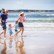 A family joyfully strolling along a sunny beach with gentle ocean waves.